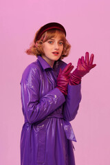 Young pretty girl in fashionable retro-style clothes, violet headband amd raincoat and gloves. Violet background. Beautiful lighting, unusual portrait
