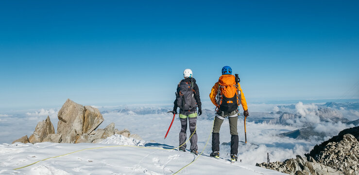 Couple connected team rope  with climbing harness dressed mountaineering clothes with backpacks and ice axes enjoying views ascending Mont Blanc (Monte Bianco) summit near Aiguille du Midi, France.