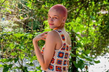 Portrait of a girl with very short hair, dyed pink. Portrait of girl wearing crochet outfit. Portrait of almost bald girl.