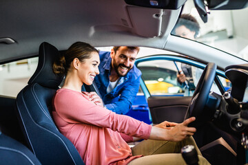 Beautiful young couple at car showroom choosing a new car to buy.