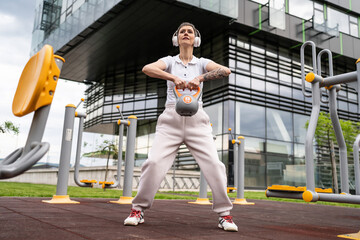 One woman modern mature caucasian female with short hair training in front of building in day with kettlebell weight at outdoor gym Sport fitness healthy lifestyle concept copy space