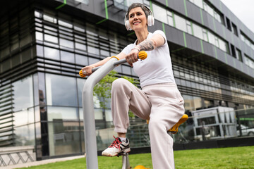 One woman modern mature caucasian female with short hair training in front of building in day on bicycle trainer machine simulator at outdoor gym Sport fitness healthy lifestyle concept copy space