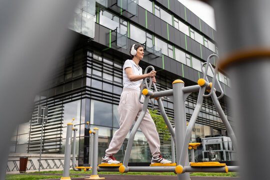 One woman modern mature caucasian female with short hair training in front of building in day on orbitrack elliptical trainer machine simulator at outdoor gym Sport fitness healthy lifestyle concept