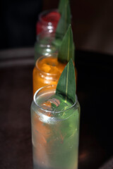 Four multi-colored cocktails in a black dark bar under a beam of light.