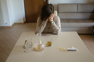 Desperate woman with hands on head and leaning on the table at home after consuming psychiatric...
