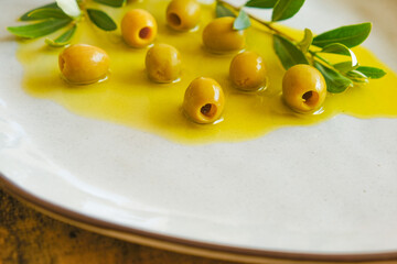 Olives and olive oil.Green olives and olive branch in olive oil in a ceramic gray plate close-up .Cold Pressed Organic Natural Oil