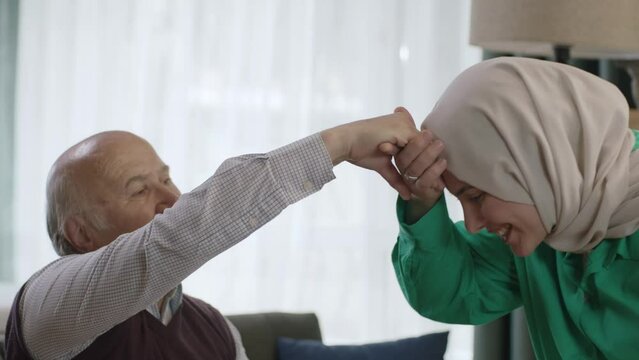 A woman in hijab visits her father during Eid Mubarak (Turkish Ramadan or Şeker Bayram). The woman kisses her father's hand to show respect. Muslim holiday traditions concept.Close up version.