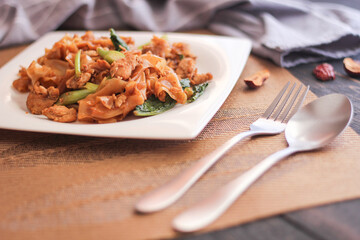 Stir fried Noodle with black soy sauce served in a white plate. on the black wooden table or what we call 