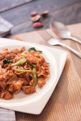 Stir fried Noodle with black soy sauce served in a white plate. on the black wooden table or what we call 