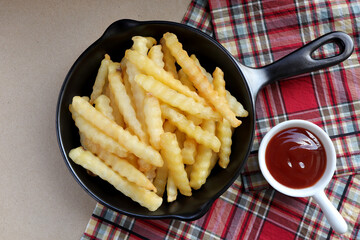Tasty french fries or potato chips in a black frying pan with ketchup on the table. from above. empty space for text. 