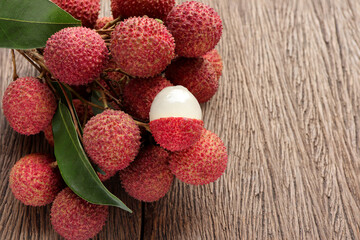 Fresh ripe lychee fruit and peeled lychee with green leaves on wooden background. rustic style, from above