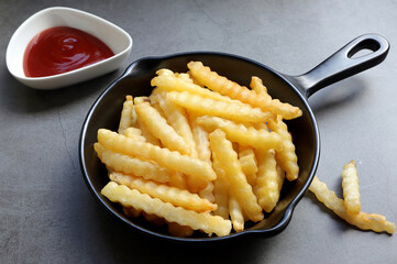 Tasty french fries or potato chips in a black frying pan with ketchup on the table. from above. empty space for text. 