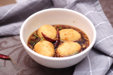 Egg with Tamarind Sauce in a white plate served on a wooden table with coriander sprinkles, is a popular local dish that Thai people eat.