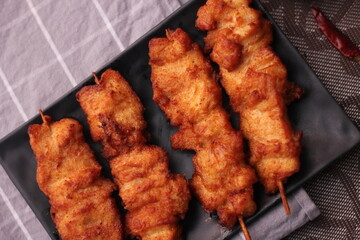 Fried pork skewers served on a black plate.