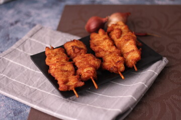 Fried pork skewers served on a black plate.