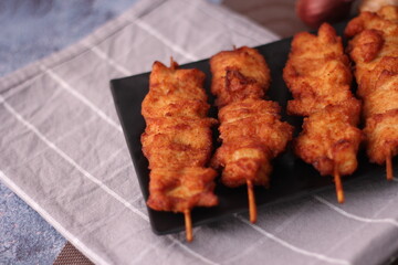 Fried pork skewers served on a black plate.