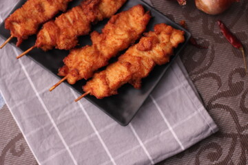 Fried pork skewers served on a black plate.