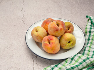 Group of fresh ripe peaches fruit on a white dish and cloth over the cement floor background