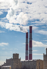 CHP in the city. Smoke rises into the sky from the heat pipes of the power plant. Pipe of combined heat and power plant CHP or cogeneration against background of multi-storey residential buildings