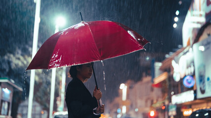 In the rain, an Asian woman holds an umbrella.