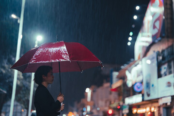 In the rain, an Asian woman holds an umbrella.