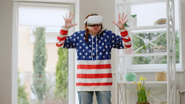 Frightened mature woman in VR headset gesturing screaming standing at home indoors. Fornt view portrait of Caucasian female retiree gaming online in augmented reality. Lifestyle and leisure