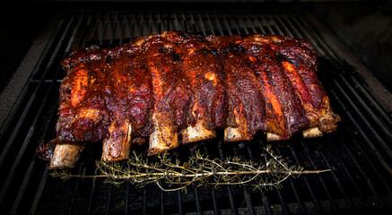 Rack of beef ribs cooking on a barbecue with a sprig of rosemary