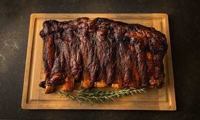 Rack of beef ribs cooked and placed on a wood cuttingboard with a sprig of rosemary