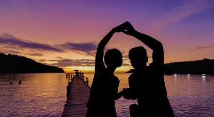 Silhouette middle aged couple relaxing on wooden pier in holiday at koh kood ,Thailand.