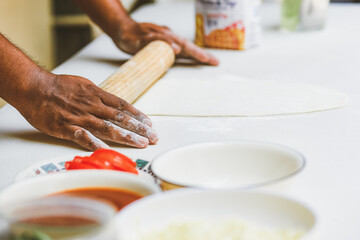 Latino man preparing artisanal pizza. Making pizza in a wood oven, vegan pizza, pizza amazon. Cheese and tomato on pizza. Fast food preparation. Tomato sauce, cheese and tomato.