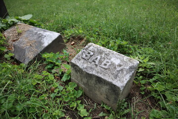 A grave marked for a baby sits in a graveyard or cemetery surrounded by green grass for baby loss...