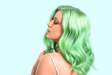 Beautiful young woman with green hair on light color background