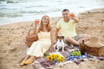 Mature couple with dog having picnic near sea on summer day