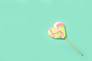 Sweet lollipop in shape of heart on color background