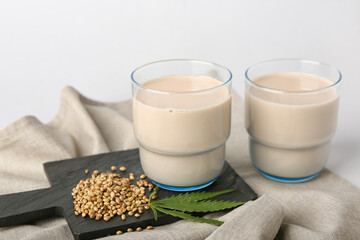 Glasses of hemp milk and seeds on white background