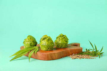 Wooden board with cannabis muffins, leaves and seeds on color background
