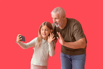 Little girl with her grandfather taking selfie on red background