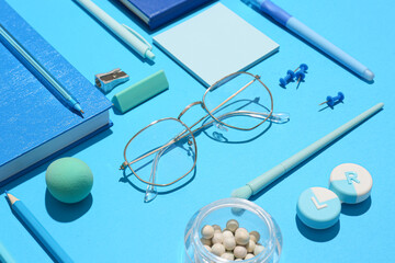 Stylish eyeglasses with stationery and cosmetic products on blue background