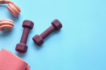 Dumbbells, fitness mat and stylish headphones on color background