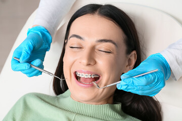 Beautiful woman with dental braces visiting dentist in clinic, closeup - obrazy, fototapety, plakaty