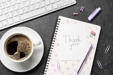 Paper sheet with text THANK YOU, stationery, cup of coffee and computer keyboard on dark background