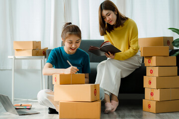 Freelance 2 Asian girls working as a team SME business office to organize and check orders for customers and online delivery for packing with parcel boxes.