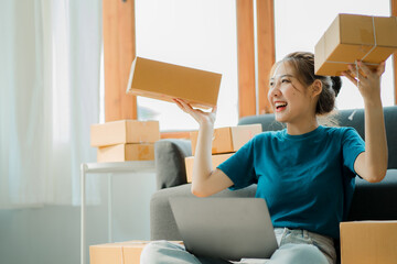 Young businesswoman in Asia packs products in cardboard boxes and sends customers work from home with laptops to take orders. small business owner start online marketing sme independent business idea