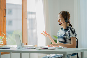 Young Asian student wearing headphones using a laptop Write a note about learning a language. View...