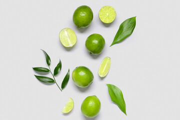 Fresh juicy limes and leaves on light background
