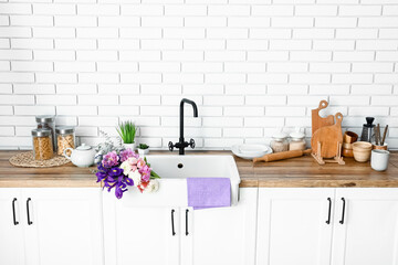 Ceramic sink with beautiful flowers and kitchen utensils on counters near white brick wall