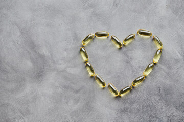 Fototapeta na wymiar Heart-shaped omega-3 capsules on a gray background. The concept of medicine and healthy living. Top view.