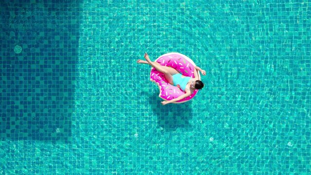 Top view of young asian woman in swimsuit on the pink donut lilo in the swimming pool.