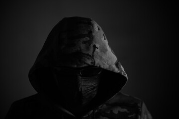 Stylish man in dark hoodie with black glasses and mask dark background, hacker, attacker and bandit.