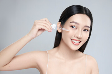 Beautiful young asian woman apply facial serum isolated on light grey background. Skin care and...